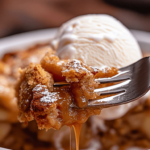 Alt Text: Fork slicing into warm caramel apple dump cake with ice cream